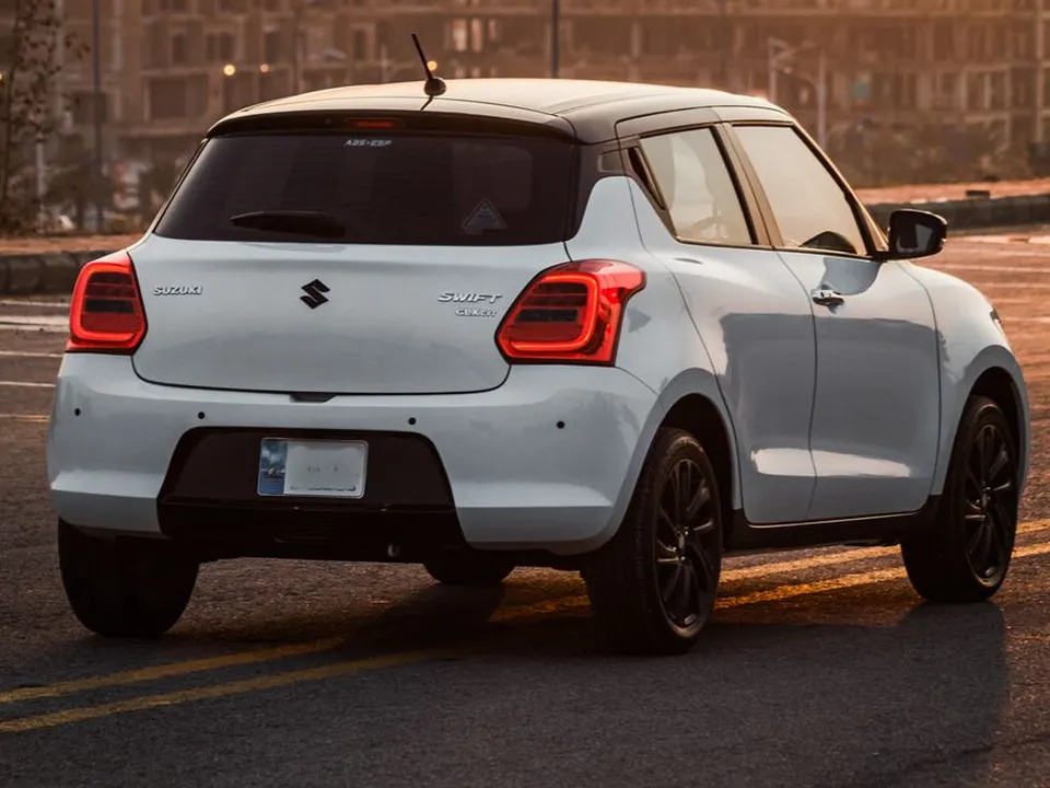 White 2025 Suzuki Swift, the manual driving school car, on a Lahore road at sunset